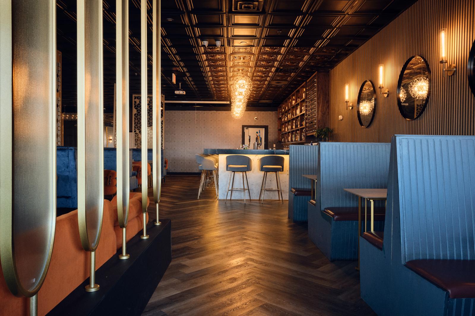 Full dining room — gold columns, herringbone floor, glowing bar in depth