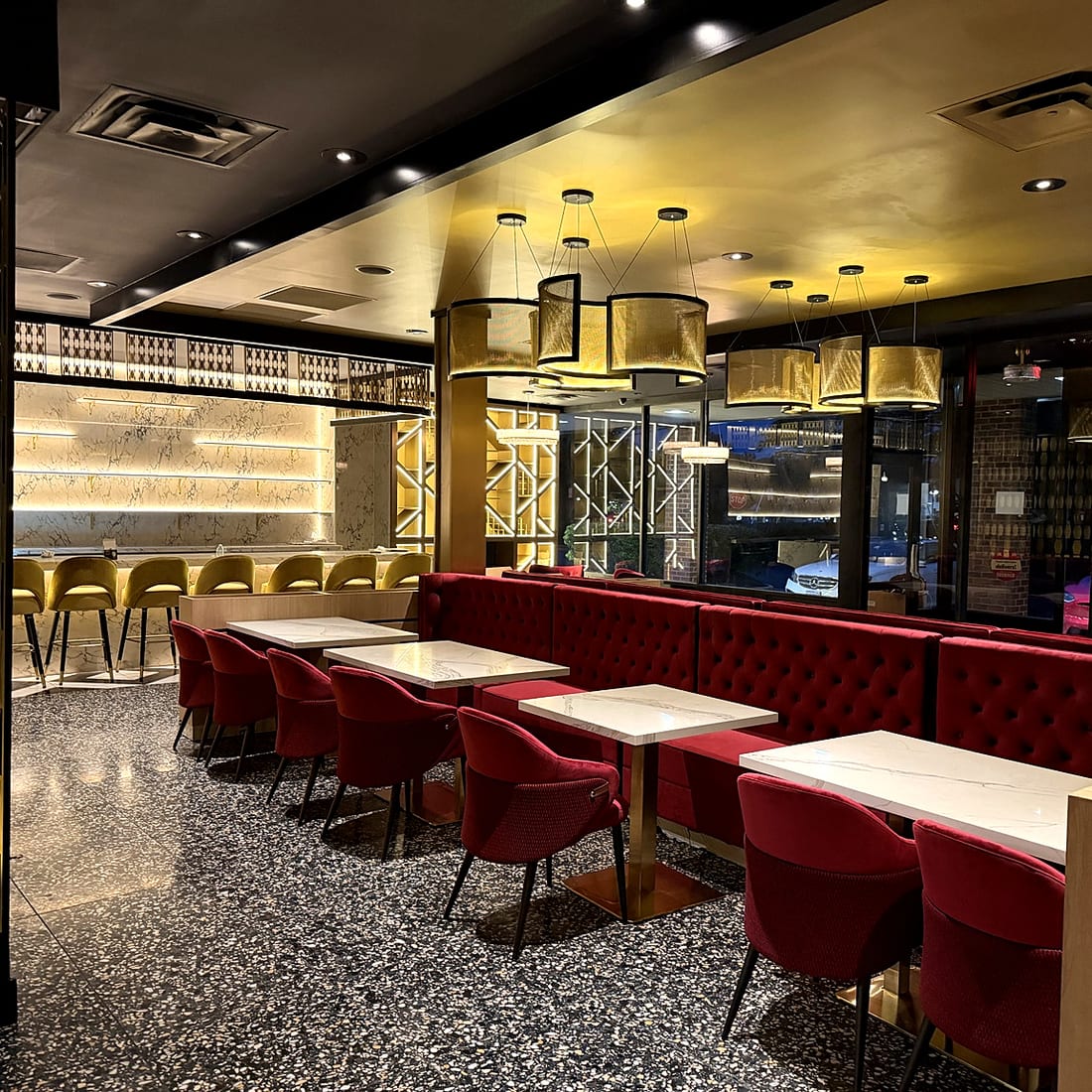 Red banquettes under gold drum pendants with marble bar behind